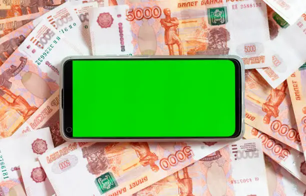 Photo of A smartphone with a green screen on the background of Russian money with a face value of 5000 rubles. The concept of wealth, success, modern technology, earning through the Internet.