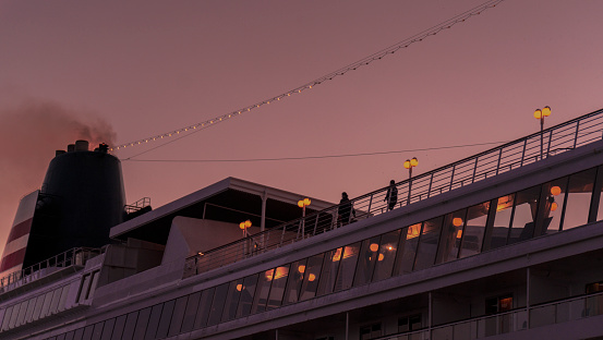 At dusk, looking up at the brightly lit cruise ship sailing under the purple sky over Yokohama harbor at sunset, there are some people on the cruise ship, both romantic and lonely.