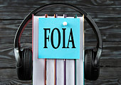 FOIA - word on a blue piece of paper on the background of a stack of books and headphones. Freedom of Information Act concept