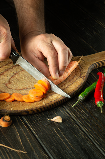 The chef cuts carrot on a cutting board for cooking ajika. Peasant delicious food.