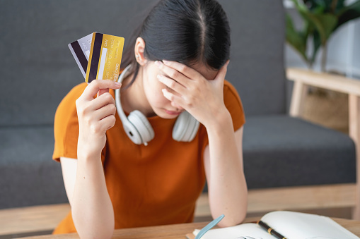 Financial owe, hand of asian woman sitting, holding many credit card, stressed by calculate expense from invoice or bill, no money to pay, mortgage or loan. Debt, bankruptcy or bankrupt