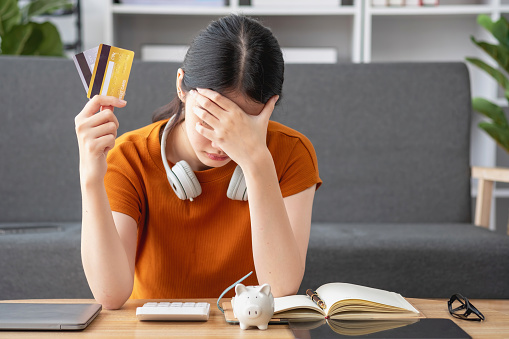 Financial owe, hand of asian woman sitting, holding many credit card, stressed by calculate expense from invoice or bill, no money to pay, mortgage or loan. Debt, bankruptcy or bankrupt