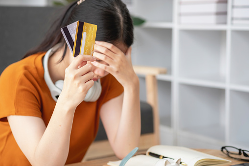 Financial owe, hand of asian woman sitting, holding many credit card, stressed by calculate expense from invoice or bill, no money to pay, mortgage or loan. Debt, bankruptcy or bankrupt