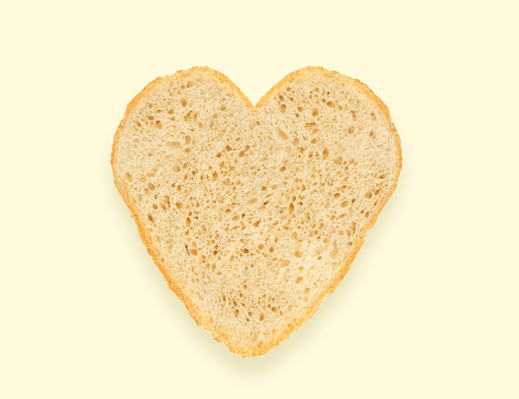 Abstract creative heart shaped cut-out from slice of white bread on light yellow background. Minimal flat lay. love food concept