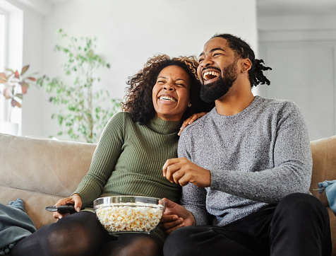 Portrait of a happy young couple watching tv together at home. Shot of a couple resting on the couch watching television