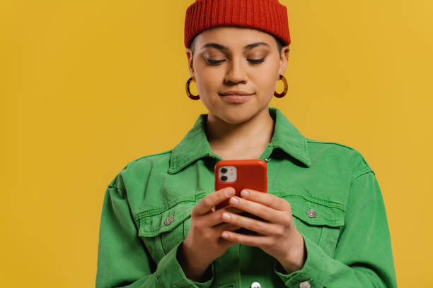 istock Fashionable young woman using smart phone while standing against yellow background 1495822853