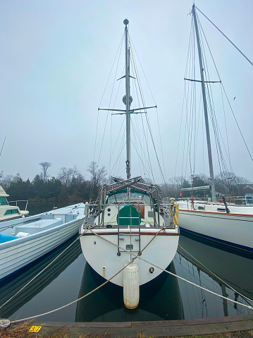 Vertical view of the back of a sailboat tied up in a marina on a foggy winters morning.
