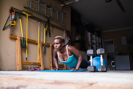 A mid adult African woman doing some exercises in her garage at home. Woman keeping fit and healthy by doing a home workout. Push up's are a great upper body exercise.