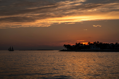 Wide angle view of a sail boat sailing towards Sunset Key at sunset from Mallory Square, Key West, Florida.