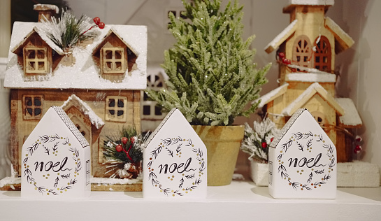 Retail display of multicolored ceramic products of miniature beach huts, house and potted plant for Christmas decoration on the shelf