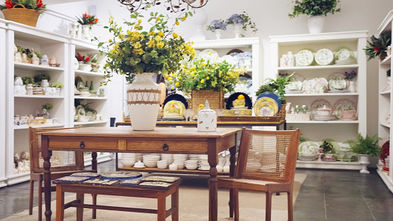 Interior of a modern ceramics store with wooden table and chairs and products displayed on racks around