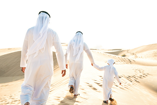 Three generation family making a safari in the desert of Dubai wearing white kandura outfit. Grandfather, son and grandson spending time together in the nature.