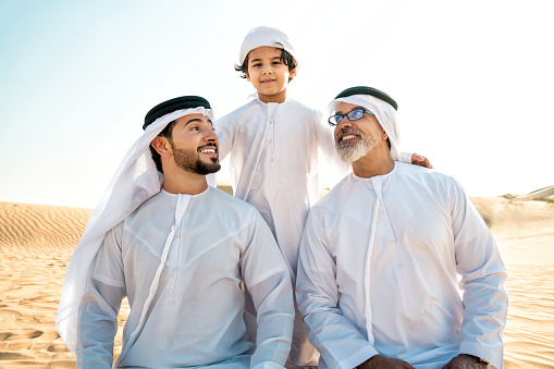 Three generation family making a safari in the desert of Dubai wearing white kandura outfit. Grandfather, son and grandson spending time together in the nature.