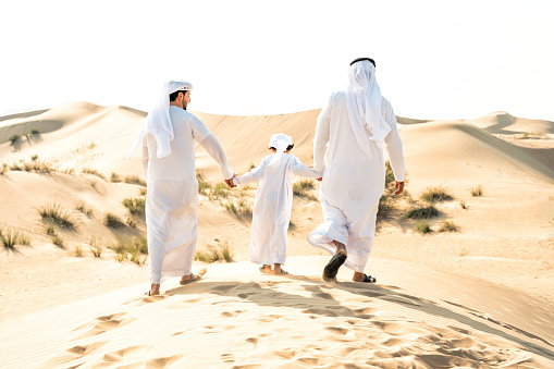 Three generation family making a safari in the desert of Dubai wearing white kandura outfit. Grandfather, son and grandson spending time together in the nature.