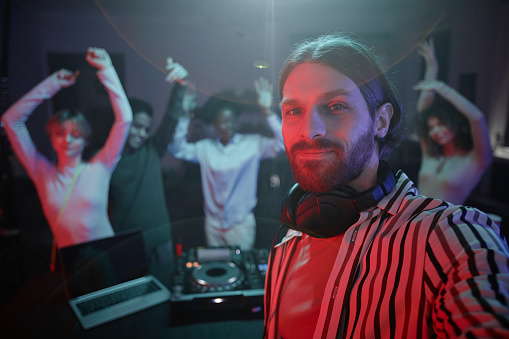 POV of long haired DJ taking selfie photo at retro disco party with people dancing in background, copy space