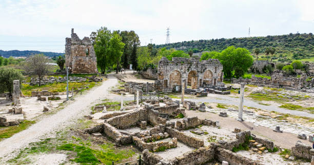 The stunning ancient city of Perge contains some of the most beautiful Hellenistic and Roman Ruins in Turkey and is easily accessible from the modern city of Antalya. The city is rich with history as Alexander the Great once strode through its gates, and the Apostle Paul preached there on his missionary journeys. Prominent features of the site include a remarkably well-preserved theater, the best-preserved Roman Stadium in Western Turkey, exquisite Roman Baths, towering Hellenistic Defenses, and long rows of beautiful colonnaded streets. The Archaeological Site of Perge was added to the UNESCO World Heritage Tentative List in 2009. vista aérea de antalya anfiteatro de la ciudad antigua de perge, sitio histórico ciudad antigua de perge antalya, sitios históricos en turquía, ciudad antigua mejor conservada, vista aérea de la ciudad antigua de perge, mejor ciudad antigua romana hel