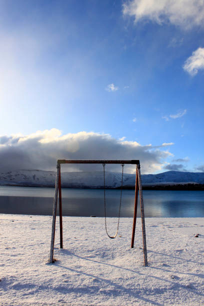 precarious wooden hammock on the shore of Lake Caviahue in Neuquén Argentina, snowy ground, with cloudy sky and snowy mountains in the background vertical stock photo
