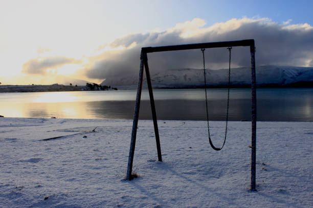 precarious wooden hammock on the shore of Lake Caviahue in Neuquén Argentina, snowy ground, with cloudy sky and snowy mountains in the background stock photo