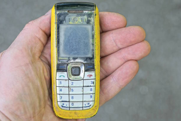 hand holds one old yellow black mobile phone on the street against the gray background