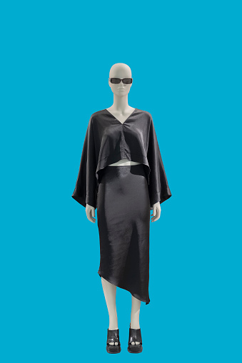 Full length image of a female display mannequin wearing fashionable black suit with blouse and skirt isolated on a blue background