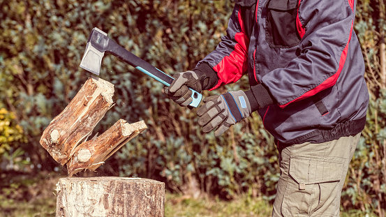 Firewood preparation using modern ax tool with wedge shaped bit and plastic haft in green garden. Energy crisis