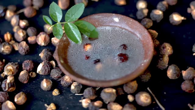 Cinematic dolly shot of Sapindus mukorossi or soapnuts or areetha on a black-colored surface along with its fermented water used for hair care and cosmetics.