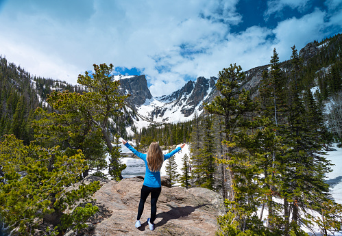 Joyful Girl with raised hands relaxing on top of the mountain, looking at beautiful summer  landscape. Dream Lake on Emerald Lake Trail. Rocky Mountains National Park, Colorado, USA.