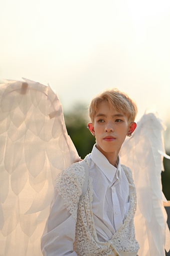 Portrait fashion in vertical with attractive teenage boy in stylish white outfit and angel wings.