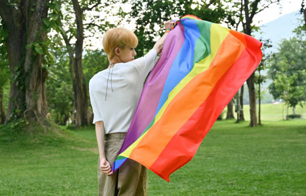 rückansicht mit einem jungen asiatischen jungen, der die regenbogenflagge schwenkt, unterstützen sie die gleichstellung von lgbt-menschen. - adolescence flag university people stock-fotos und bilder