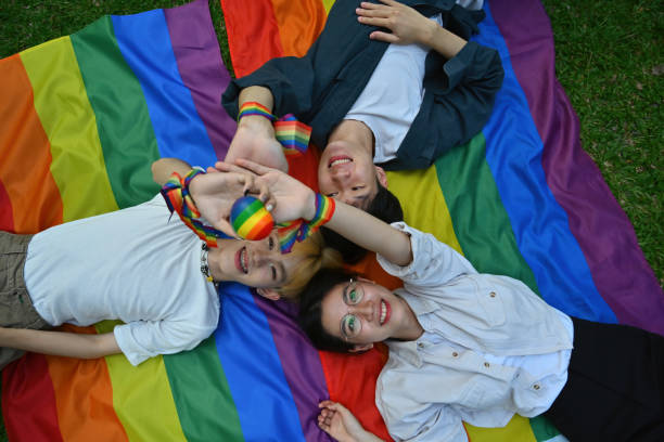 draufsicht mit einer gruppe von lgbt-teenagern, die ein regenbogenherzmodell halten, während sie sich auf regenbogenflaggen legen. - adolescence flag university people stock-fotos und bilder