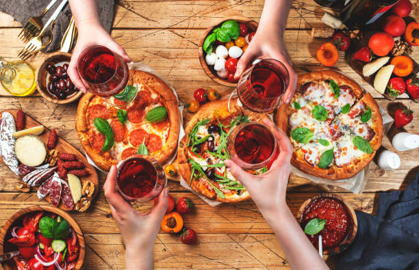 pizzaparty mit freunden. draufsicht leute mit gläsern mit rotwein, rustikaler holztisch mit heißen pizzen, italienischen vorspeisen, salaten, käse, obst und beeren. familienessen mit fast food - italienische küche stock-fotos und bilder