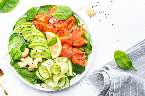 Keto salad with salmon, avocado, spinach, cucumber, sesame seeds  and cashew nuts. Low-carbohydrate breakfast rich in healthy fats. White table background, top view