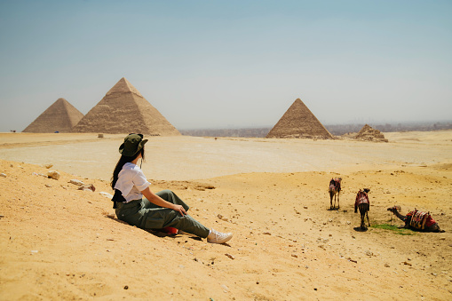 Egypt, Cairo, asian female tourist sitting  on rocks with Great Pyramid of Giza in background