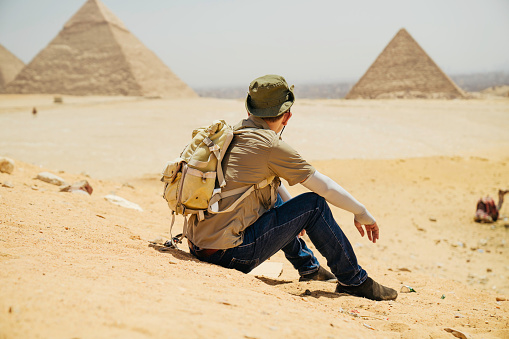 Egypt, Cairo, asian man tourist sitting  on rocks with Great Pyramid of Giza in background