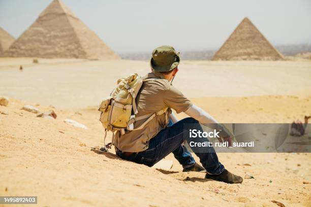 Egypt Cairo Asian Male Tourist Sitting On Rocks With Great Pyramid Of Giza In Background Stock Photo - Download Image Now
