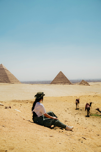 Egypt, Cairo, asian female tourist sitting  on rocks with Great Pyramid of Giza in background