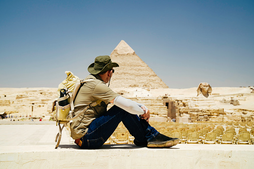 Egypt, Cairo, asian man tourist sitting  on rocks with Great Pyramid of Giza in background