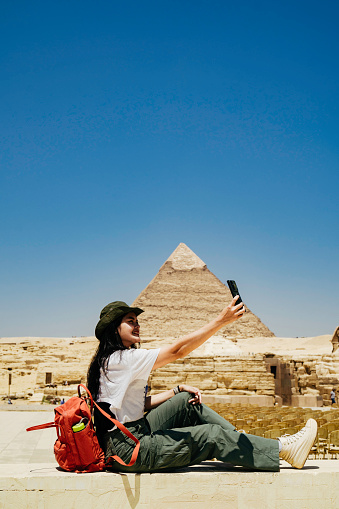 Egypt, Cairo, asian female tourist sitting  on fence with Great Pyramid of Giza in background