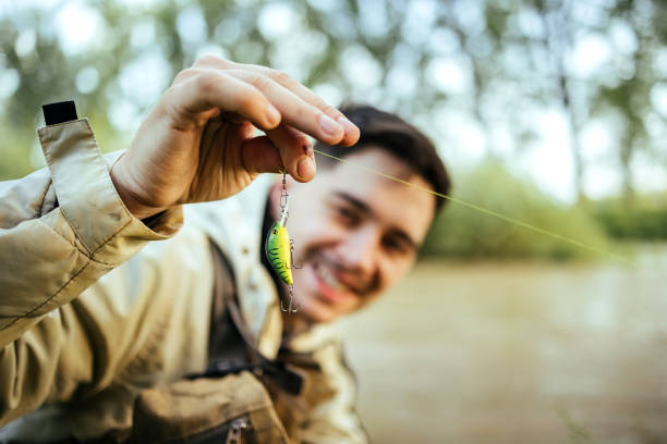 Colorful fishing lure with treble hook hanging on line above water surface. Outdoor angling equipment close-up on lake background. Sport fishing and tackle preparation concept