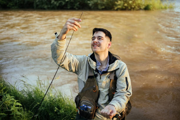 An elderly man is walking along a dirt trail in a natural setting, holding a fishing rod. He is dressed in a plaid shirt and a vest, showcasing a relaxed outdoor lifestyle. This image captures the essence of leisure and the joy of fishing in nature.