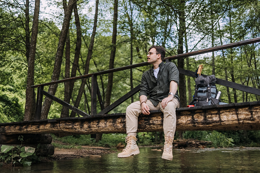 Hiking man sits on a bridge and rests