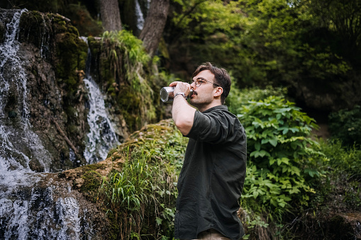 Man stands by a waterfall and drinks fresh water