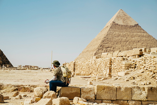 Egypt, Cairo, asian man tourist sitting  on rocks with Great Pyramid of Giza in background