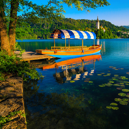 Pletna boat anchored at the pier on the lake. Pletna rowing boat and famous church in background on the small island, Bled, Slovenia, Europe