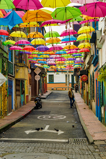 Bogota, Colombia - January 2, 2023: Tourist walks through an alleyway decorated with colored umbrellas in the La Candelaria district