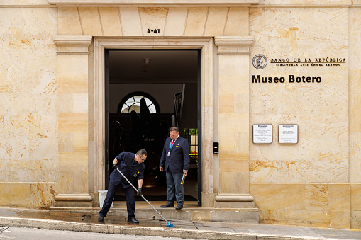 Bogota, Colombia - January 2, 2023: Man cleans the entrance path to the Botero Museum while a security guard talks to him