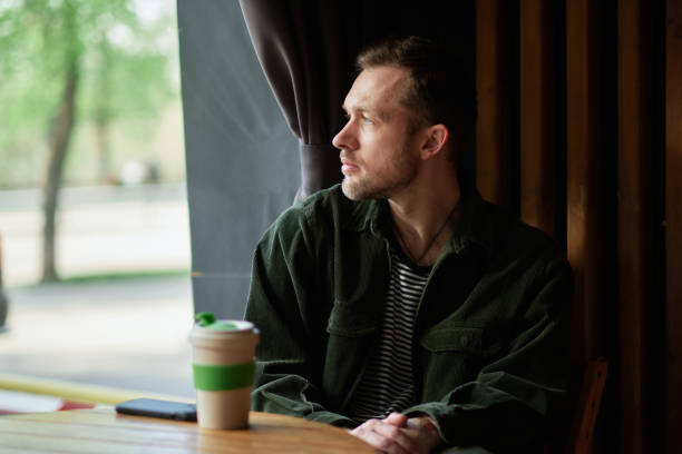 istock Young handsome man sitting in small cafe on a coffee break looking at window 1495905189