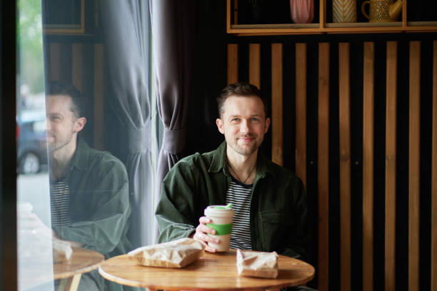 istock Young handsome man sitting in small cafe on a coffee break looking at camera 1495905485