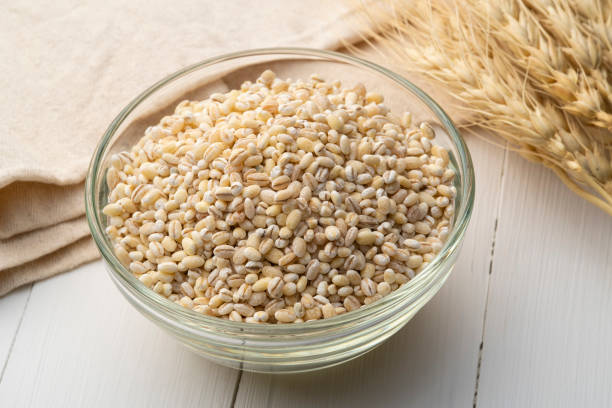 Uncooked barley, pearl barley in glass bowl on wood table