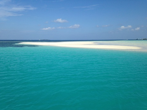 A small, sandy island surrounded by crystal clear, turquoise waters on an overcast day